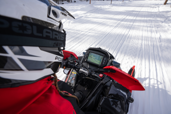 Person riding a snowmobile on a snowy trail, wearing a helmet and red jacket.