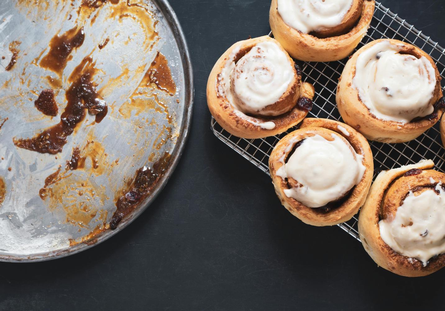Five iced cinnamon rolls on rack, empty tray beside them.