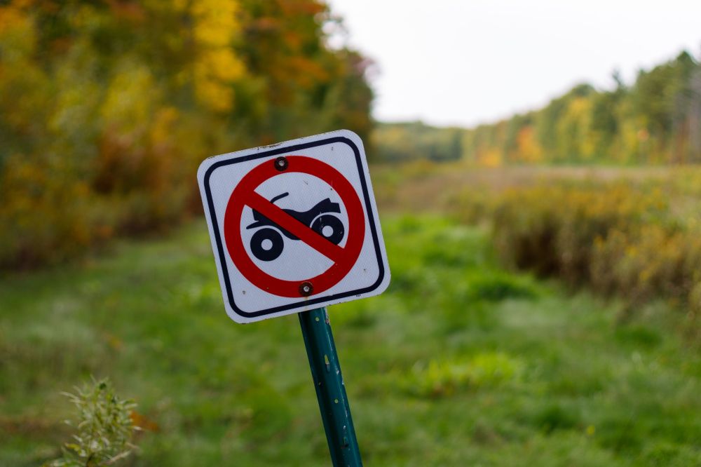No off-road vehicles sign on grassy path with trees in background.